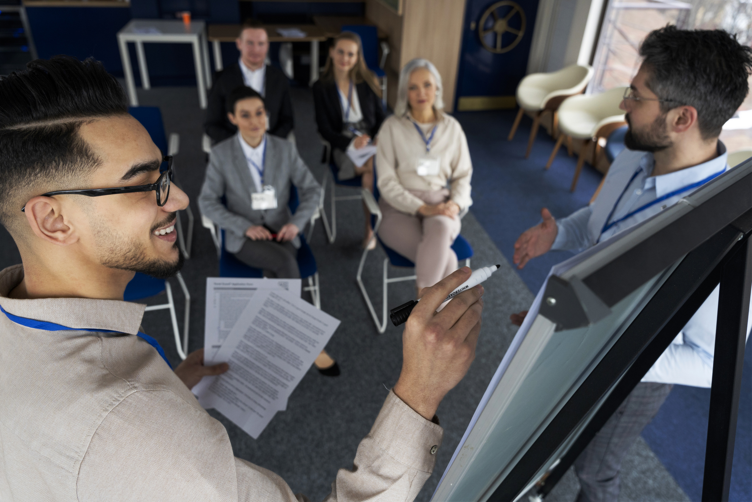 Facilitators at the front of a room with people seated in the background.